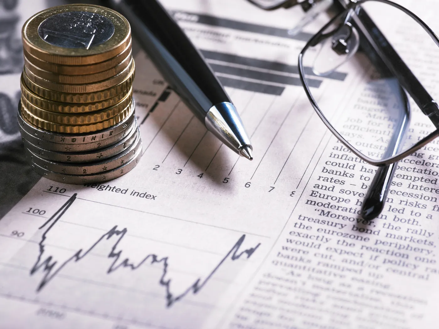Relatórios com gráficos, calculadora e moedas sobre a mesa, representando a gestão financeira de condomínios em João Pessoa